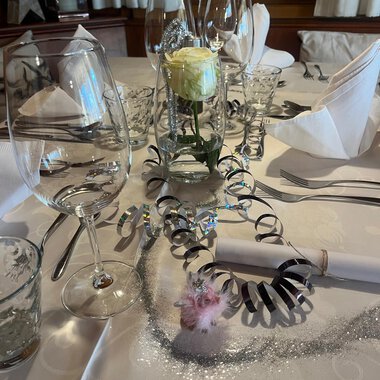 Zwei Sektgläser stoßen auf einem festlich dekorierten Tisch an. Im Hintergrund sind rote Weihnachtskugeln und goldene Dekoration zu sehen. | © Genuss- & Aktivhotel Sonnenburg