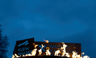 Ein Werbeschild mit der Aufschrift "Klein Walser" brennt im Dunkeln. Flammen leuchten gegen den blauen Himmel. | © Kleinwalsertal Tourismus eGen | Oliver Farys