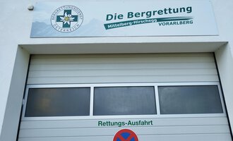 A garage door with the sign of the mountain rescue in Mittelberg-Hirschegg, Vorarlberg. The sign contains the logo and information about the rescue exit. | © Kleinwalsertal Tourismus