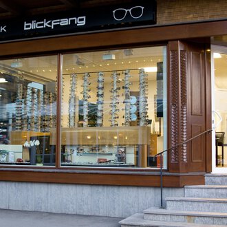 An optical shop with large windows and a selection of sunglasses. The store has a sign that says "blickfang" and has a modern design. | © Blickfang | Michael Stumpe