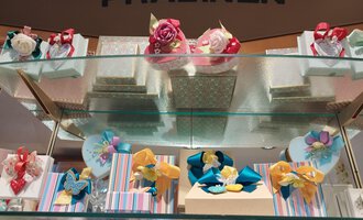 Geschenkverpackungen mit bunten Schleifen und Pralinen sind auf einem Regal angeordnet. Das Regal ist mit verschiedenen Dekorationen geschmückt. | © Kleinwalsertal Tourismus | N. Lughammer