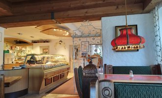 Ein gemütliches Restaurant mit einem einladenden Ambiente. Die Einrichtung ist rustikal mit einer auffälligen roten Lampe und einem Blick auf die Theke. | © Kleinwalsertal Tourismus | N. Lughammer