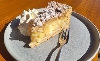 A piece of apple pie on a plate, garnished with cream. The pie has a crispy crust and is filled with pieces of apple.