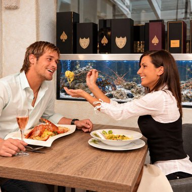 A couple is sitting in an elegant restaurant and enjoying their meal. They are smiling at each other and seem to be having a good time.
