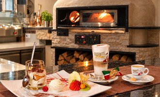 An appealing restaurant kitchen with a wood oven in the background. On the table, there is a dessert platter with ice cream and fruits, as well as two drinks.