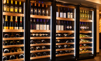 Eine stilvolle Weinschrank mit verschiedenen Flaschen Rot-, Weiß- und Schaumwein. Die Flaschen sind ordentlich in Holzregalen angeordnet und hinter Glas präsentiert.