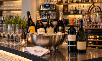 Ein eleganter Barkeeper mit verschiedenen Flaschen Schaumwein und Rotwein in einer Kühlwanne. Im Hintergrund sind Gläser und eine gut ausgestattete Bar zu sehen.