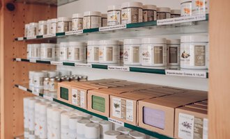 Ein Regal mit verschiedenen Behältern und Boxen für Naturprodukte. Die Produkte sind ordentlich angeordnet und beschriftet. | © Carolin Ries | www.calejofotografie.de