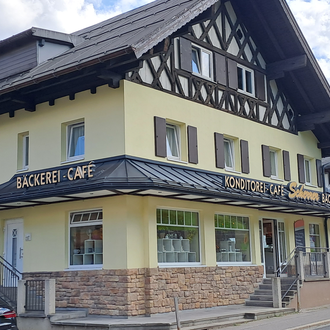 A nice café with a bakery in a traditional building. In the background, mountains and a blue sky are visible. | © Kleinwalsertal Tourismus | Steffen Stöhr