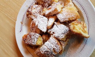 A plate with baked cake, dusted with powdered sugar. The pieces are golden brown and attractively arranged. | © Gasthof Café Alpenwald | Thorsten Alpenwald