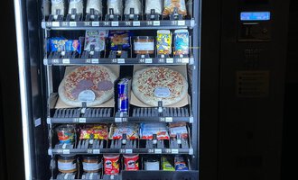 A snack vending machine with various drinks and foods. Among them are pizzas, candies, and energy drinks.