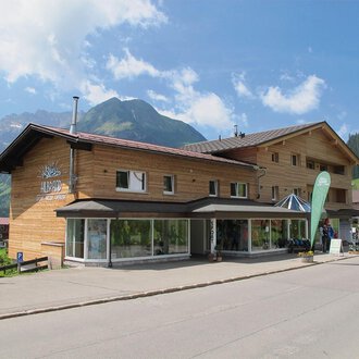 Ein modernes Holzgebäude in den Bergen. Umgeben von einer schönen Landschaft mit grünen Wäldern und Bergen. | © Sport Hilbrand GmbH