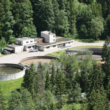 A modern wastewater treatment plant surrounded by dense forest. There are several large round basins and an administration building. | © Gemeinde Mittelberg