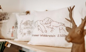 Ein Kissen mit einer Abbildung des Großen Widdersteins und der Höhe von 2.533 Metern. Im Hintergrund ist ein dekorativer Geweihkopf zu sehen. | © Herzstichle | Ninja Matt