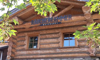 Ein gemütliches Holzhaus mit Fenster und einem dekorativen Schild. Umgeben von grünen Blättern und Bäumen. | © Kleinwalsertal Tourismus | Veronika Senn