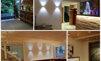 Ein modernes Innenraumdesign mit Holzelementen und warmem Licht. Verschiedene Bereiche bieten Sitzgelegenheiten und einen Fernseher. | © Hotel Bellevue | I. Malouvier