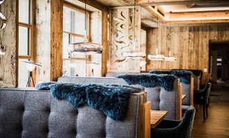 A modern restaurant with cozy benches and warm wooden decor. Large windows ensure plenty of light and an inviting atmosphere. | © Verwöhn- & Wellnesshotel Walserhof| Aileen Melucci