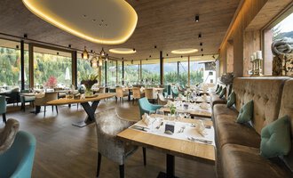 Ein modernes Restaurant mit großen Fenstern und Blick auf die Natur. Stilvolle Tische und gemütliche Sitzgelegenheiten schaffen eine einladende Atmosphäre. | © Verwöhn- & Wellnesshotel Walserhof| R. Muehlbacher
