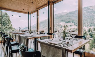 Ein modernes Restaurant mit großen Fenstern und Blick auf die Berge. Die Tische sind elegant gedeckt und schaffen eine einladende Atmosphäre. | © Naturhotel Chesa Valisa | Heldentheater