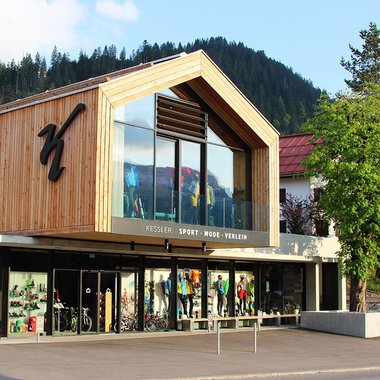 Ein modernes Sportgeschäft mit einer Holzfassade und großen Fenstern. Vor dem Geschäft sind verschiedene Sportartikel ausgestellt.