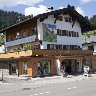 A traditional alpine house with wooden cladding and large windows. In the foreground is a bicycle and an information sign. | © Sport Pauli Matthias Bischof e.U
