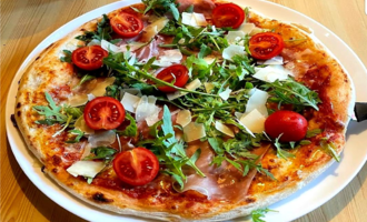 A delicious pizza with ham, cherry tomatoes, and fresh arugula. The cheese and herbs give it an appealing appearance.