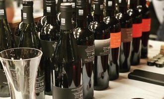 A selection of red wines in elegant bottles is on a table. In the foreground, a wine decanter is visible. | © Uusziit | Chantal Kessler