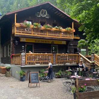 A cozy chalet surrounded by trees. Guests sit on the terrace and enjoy nature. | © Waldhaus | Yvonne Grosse
