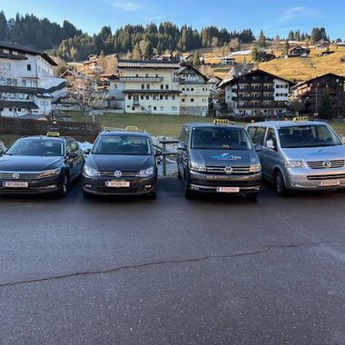 Two taxis are standing in front of a residential building. The black taxi and the white station wagon taxi are ready for passengers. | © Walser Taxi | Josef Düringer