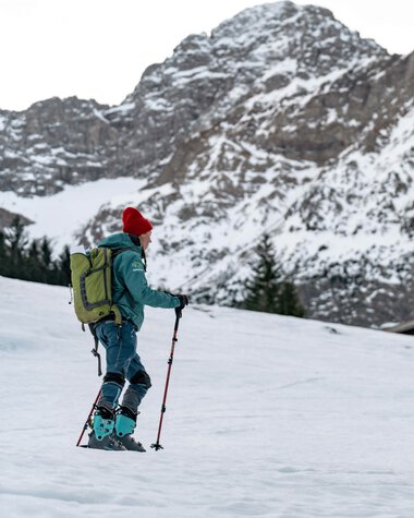 Two skiers in winter clothing on snowshoes in a snowy mountain landscape, with tall, partly snow-covered mountains in the background. | © Kleinwalsertal Tourismus eGen • Photographer: Basti Heckl