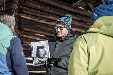 A man shows a historical photograph to a group during a cultural tour in winter. | © Kleinwalsertal Tourismus eGen • Photographer: Dominik Berchtold
