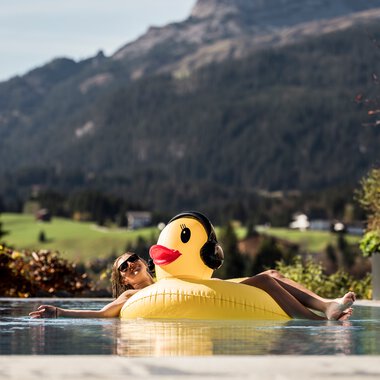 A girl relaxing on a duck-shaped pool float in a pool with mountain scenery in the background.
