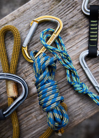 Various climbing and safety gear, including carabiners and ropes, are placed on a log at the climbing garden.