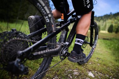 Close-up of a mountain biker riding on a singletrail in Kleinwalsertal, focusing on the pedals and chain. | © Kleinwalsertal Tourismus eGen • Photographer: Oliver Farys