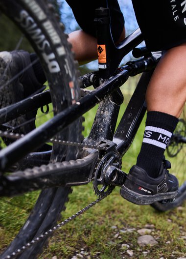 Close-up of a mountain biker riding on a singletrail in Kleinwalsertal, focusing on the pedals and chain. | © Kleinwalsertal Tourismus eGen • Photographer: Oliver Farys