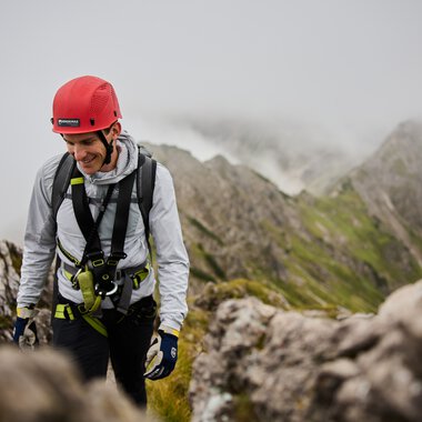 Exciting mountain climb with a smiling climber in gear and helmet in a rocky landscape. | © Kleinwalsertal Tourismus eGen • Photographer: Oliver Farys