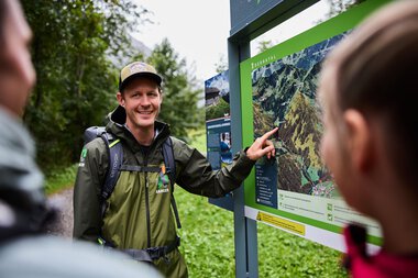 A man explains a map to a group of children in Kleinwalsertal, providing educational information about the nature reserve. | © Kleinwalsertal Tourismus eGen • Photographer: Oliver Farys