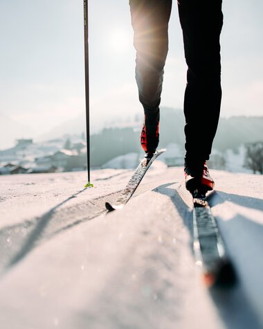 Cross-country skier on the Schwarzwasserloipe trail in Kleinwalsertal, focusing on skis and lower body, on a sunny winter day. | © Kleinwalsertal Tourismus eGen • Photographer: Oliver Farys
