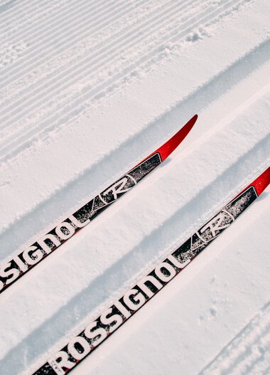 Two cross-country skis on a snowy trail in the Kleinwalsertal, showing freshly groomed snow for skiing. | © Kleinwalsertal Tourismus eGen • Photographer: Oliver Farys