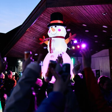 Große Schneemänner-Deko auf einer Winterveranstaltung im Kleinwalsertal, umgeben von Kindern, die zum Schnee-Fest jubeln. | © Kleinwalsertal Tourismus eGen • Fotograf: Oliver Farys