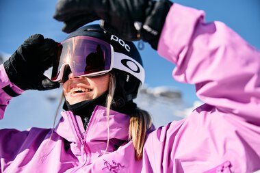 Young woman skiing in winter, wearing pink ski jacket, helmet, and goggles, smiling | © Kleinwalsertal Tourismus eGen • Photographer: Oliver Farys