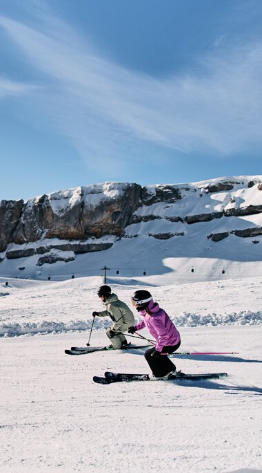 Two children skiing on a snowy slope in front of a mountain landscape in Kleinwalsertal, under a blue sky with clouds. | © Kleinwalsertal Tourismus eGen • Photographer: Oliver Farys