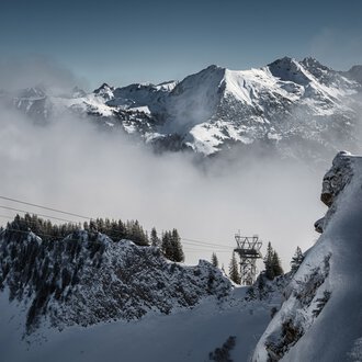 Snow-covered mountains with fog in a winter landscape and forest in the foreground. | © Kleinwalsertal Tourismus eGen • Photographer: Robert Niederwolfsgruber