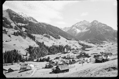 Historical black and white photo of the village Hirschegg in Kleinwalsertal featuring a church, surrounded by mountains and meadows in the Alps. | © Kleinwalsertal Tourismus eGen • Karl Max Kessler Archiv