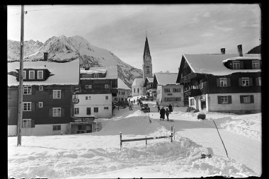 Schneebedeutes Mittelberg mit Kirche im Hintergrund, umgeben von Bergen, historische Schwarz-Weiß-Fotografie. | © Kleinwalsertal Tourismus eGen • Karl Max Kessler Archiv