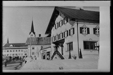 Historical black-and-white photo of a shoe and fashion store in the center of Riezlern, with a man and woman outside the shop in the snow. | © Kleinwalsertal Tourismus eGen • Karl Max Kessler Archiv