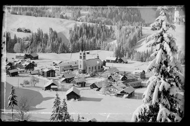 Historical photo of Riezlern covered in snow, with a church in the center, surrounded by mountains. | © Kleinwalsertal Tourismus eGen • Karl Max Kessler Archiv