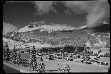 Black and white photo of Riezlern at 1,100 meters altitude, surrounded by snowy mountains and pine trees in winter. | © Kleinwalsertal Tourismus eGen • Karl Max Kessler Archiv