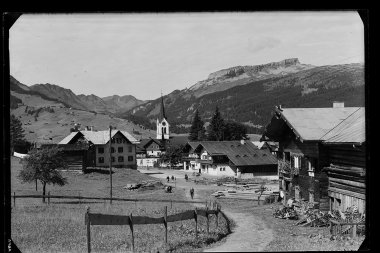 Historical photo of Riezlern with a church tower in the center, surrounding buildings, and mountains in the background. | © Kleinwalsertal Tourismus eGen • Karl Max Kessler Archiv