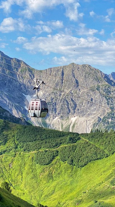Summer Kanzelwand cable car with gondolas in the alpine landscape, green hills, mountains, and blue sky. | © Oberstdorf · Kleinwalsertal Bergbahnen